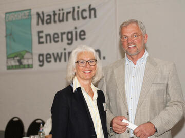 Dirk und Thoma Ketelsen stehen nebeneinander vor einer Wand, an der steht: „Natürlich Energie gewinnen“. Beide lächeln.