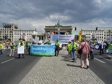 Menschen demonstrieren vor dem Berliner Tor. Sie halten ein Banner mit der Aufschrift „Natürlich Energie gewinnen“ und dem Dirkshof-Logo.
