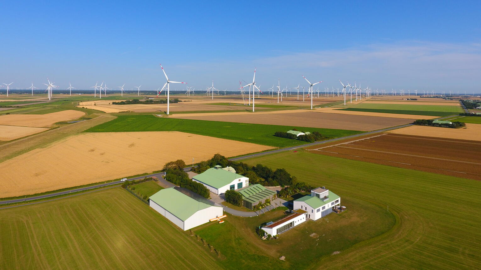 Der Dirkshof inmitten blühender Felder unter blauem Himmel, im Hintergrund einzelne Windräder.